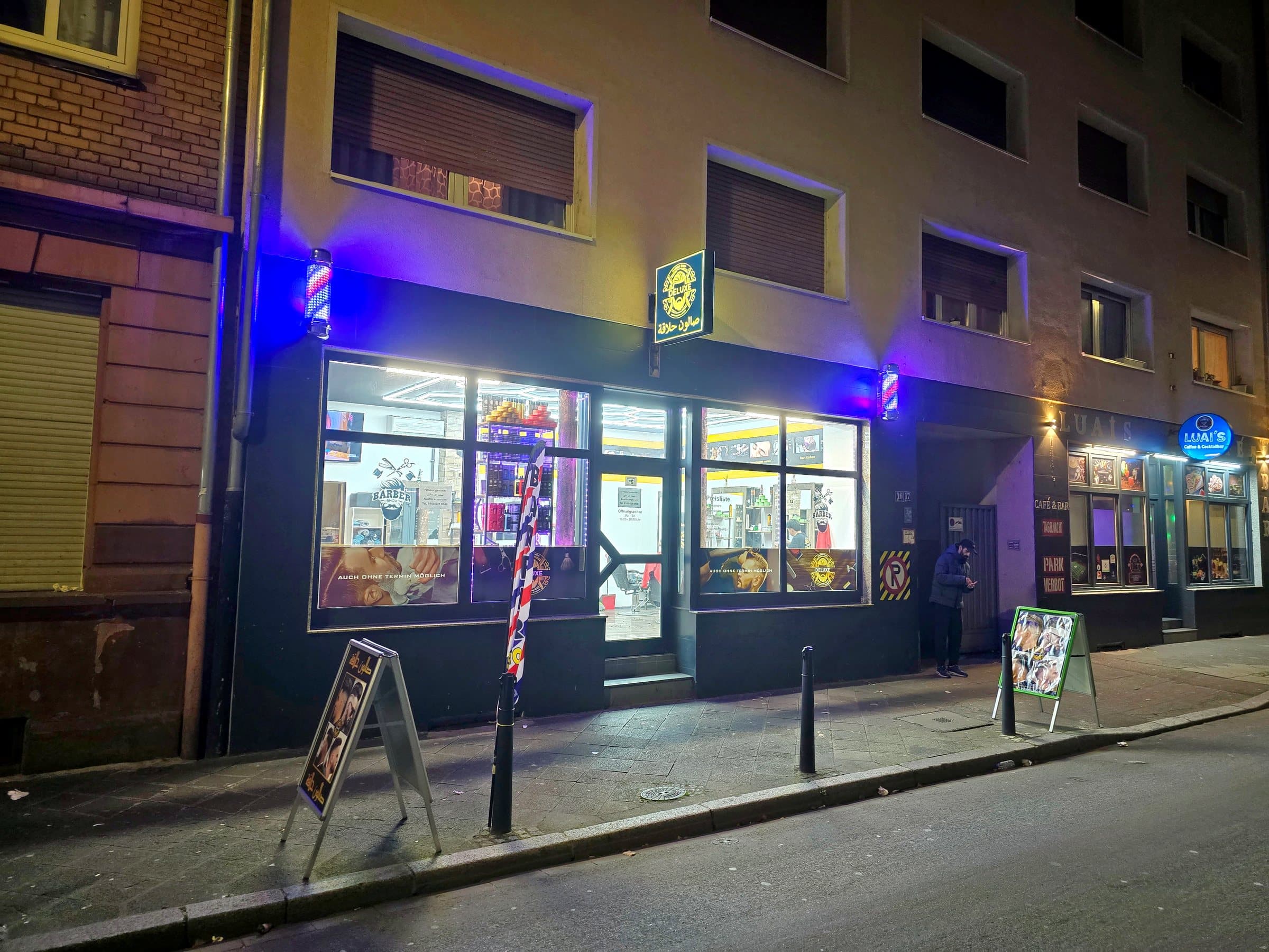 Ladenfront von Deluxe in J2, 16 am Abend, mit beleuchteten Barber-Poles